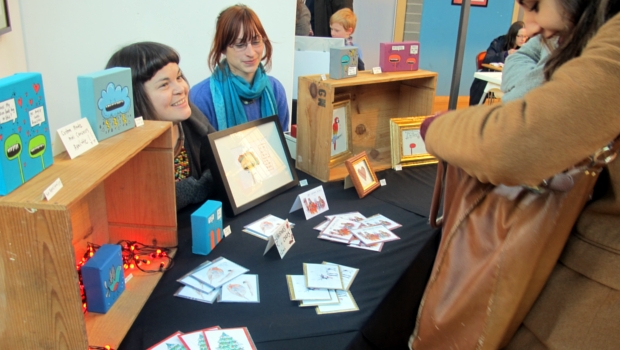 Customers and stallholders chat at an Out of the Blue Arts Market, where framed pictures and postcards are on sale.
