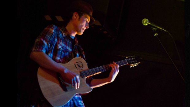 Musician Tomlin Leckie plays guitar on stage.