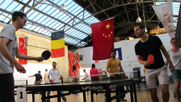 Table tennis players compete in The Out of the Blue Drill Hall underneath various flags of the world.