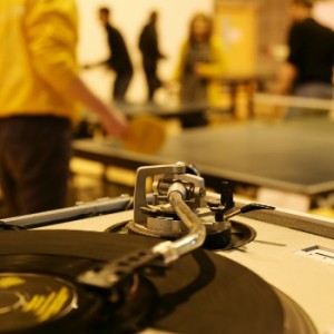 Table tennis players compete in background at a Wiff Waff Wednesday event while a vinyl record spins in the foreground.