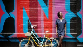 Jools Walker leans against a brightly coloured wall with a bicycle