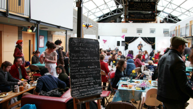 The Drill Hall Arts Cafe Bruncheon lunch menu surrounded by a busy crowd while a guitarist plays in the background