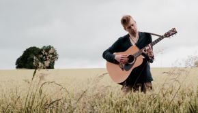 Geroge Francis playing a guitar in a field
