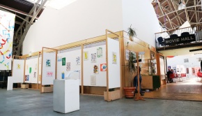 Exhibition wall near the front entrance, with the cafe and main hall in the background