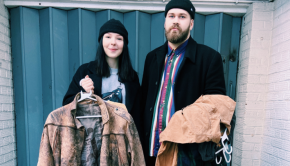 Two people holding clothing items in front of a warehouse door